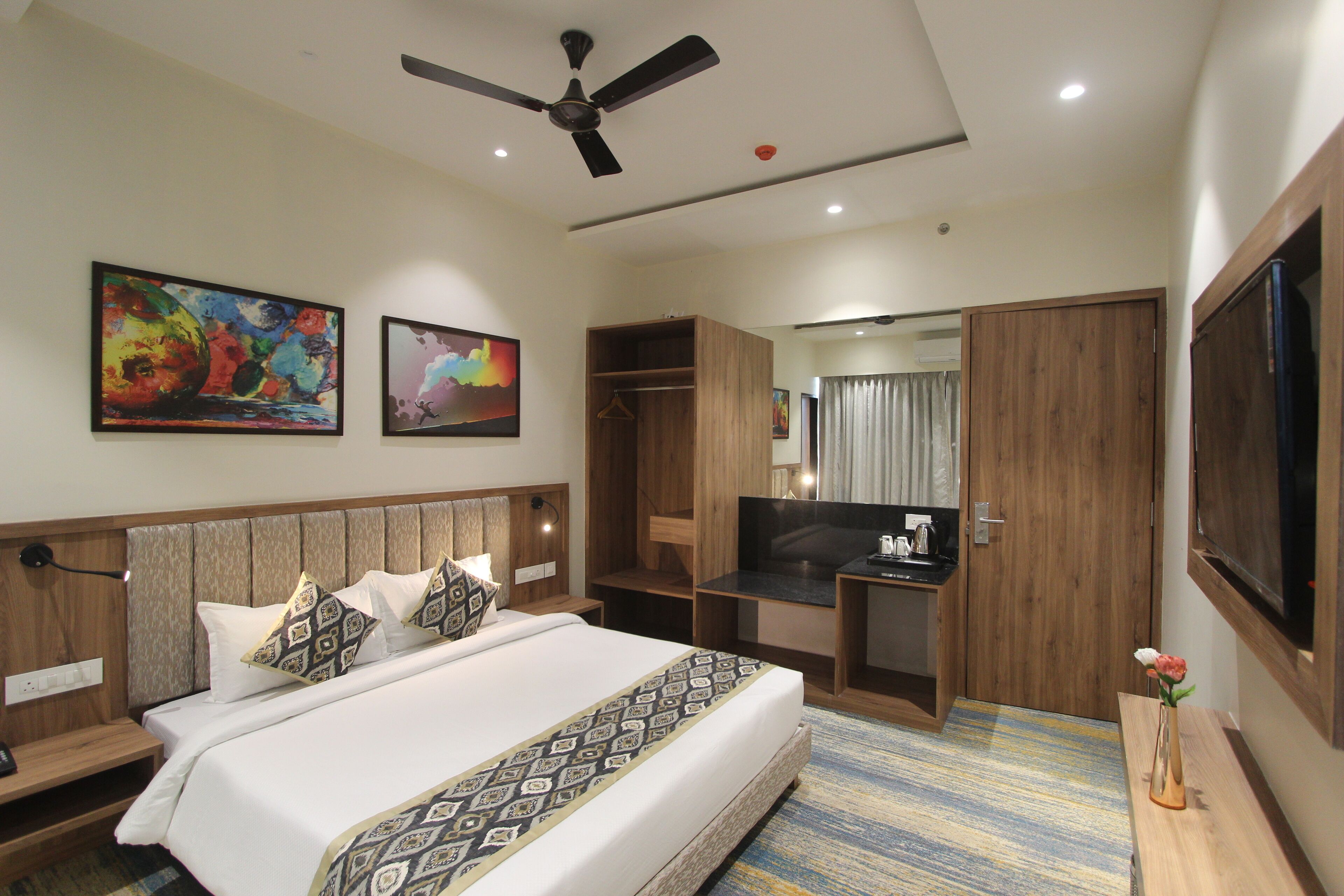 A hotel room with a bed, a desk, a wardrobe, a TV, and two paintings on the wall.