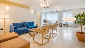 A modern living room with a blue sofa, wicker chairs, a coffee table, and a dining area with a laptop. - Granada Suites by Olala Homes (Granada)
