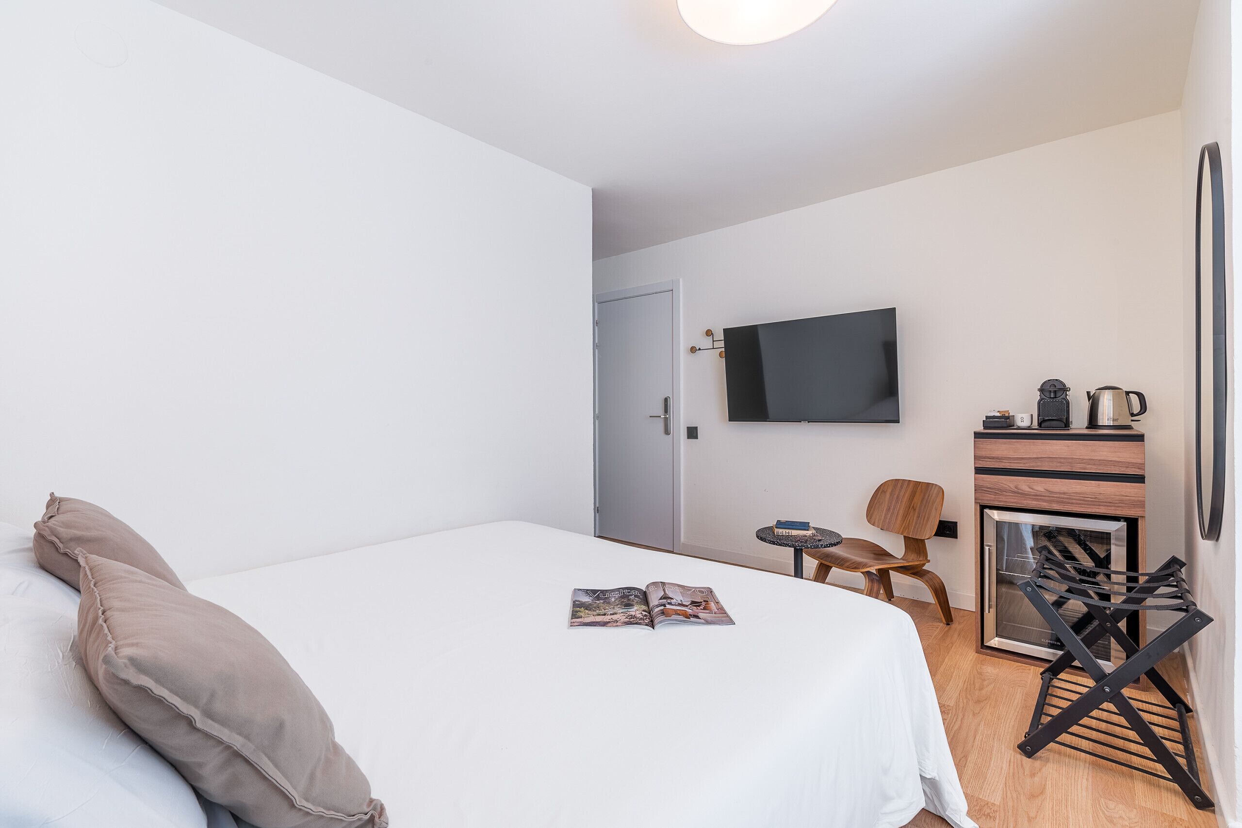 Una habitación de hotel moderna con cama, televisión, una mesita con silla y una kitchenette.