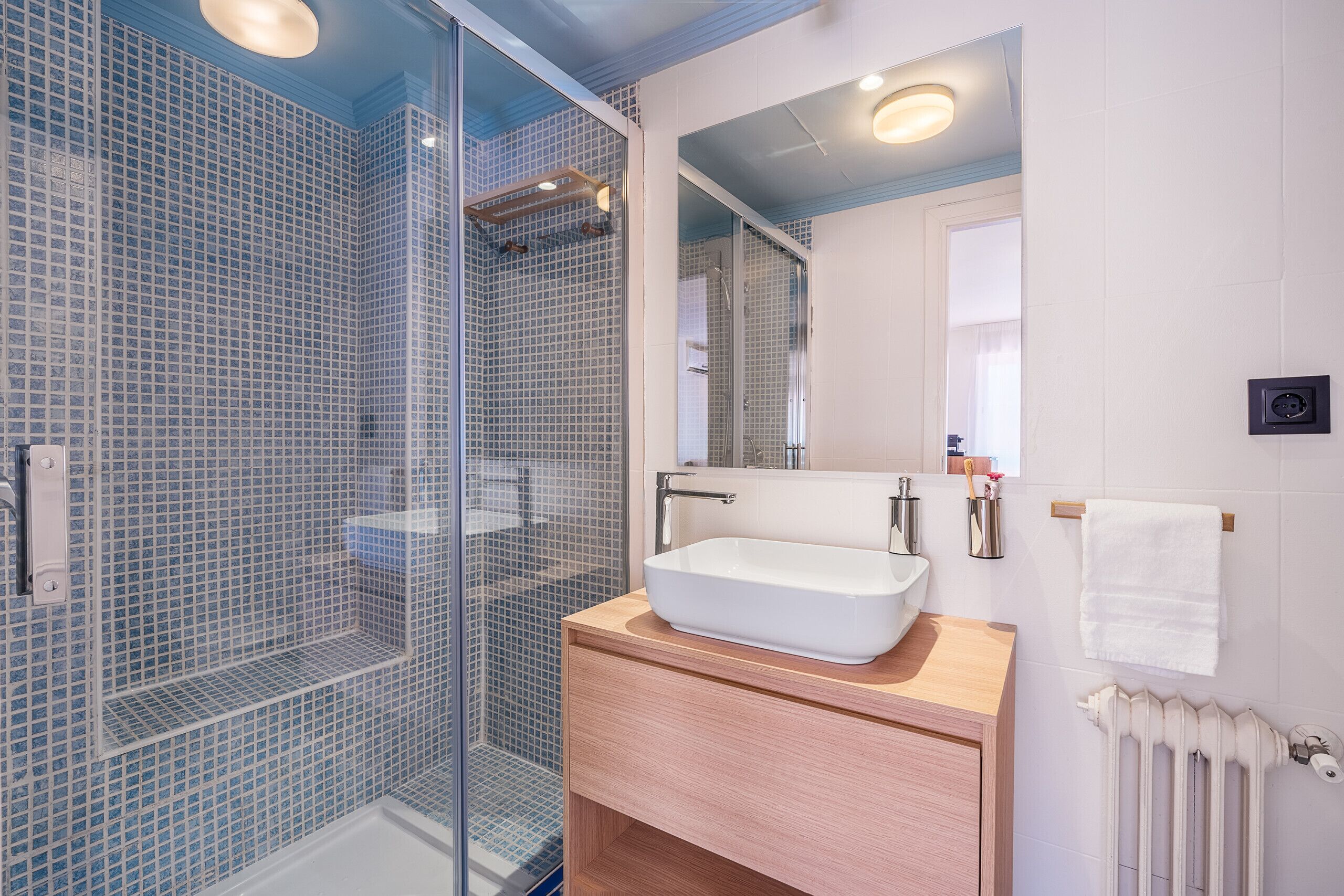 A modern bathroom with a glass-enclosed shower, a white sink, and a wooden vanity.