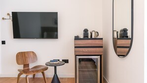 A modern room with a flat-screen TV mounted on the wall, a wooden chair, a small round table, a built-in coffee machine, and a mirror. - Granada Suites by Olala Homes (Granada)