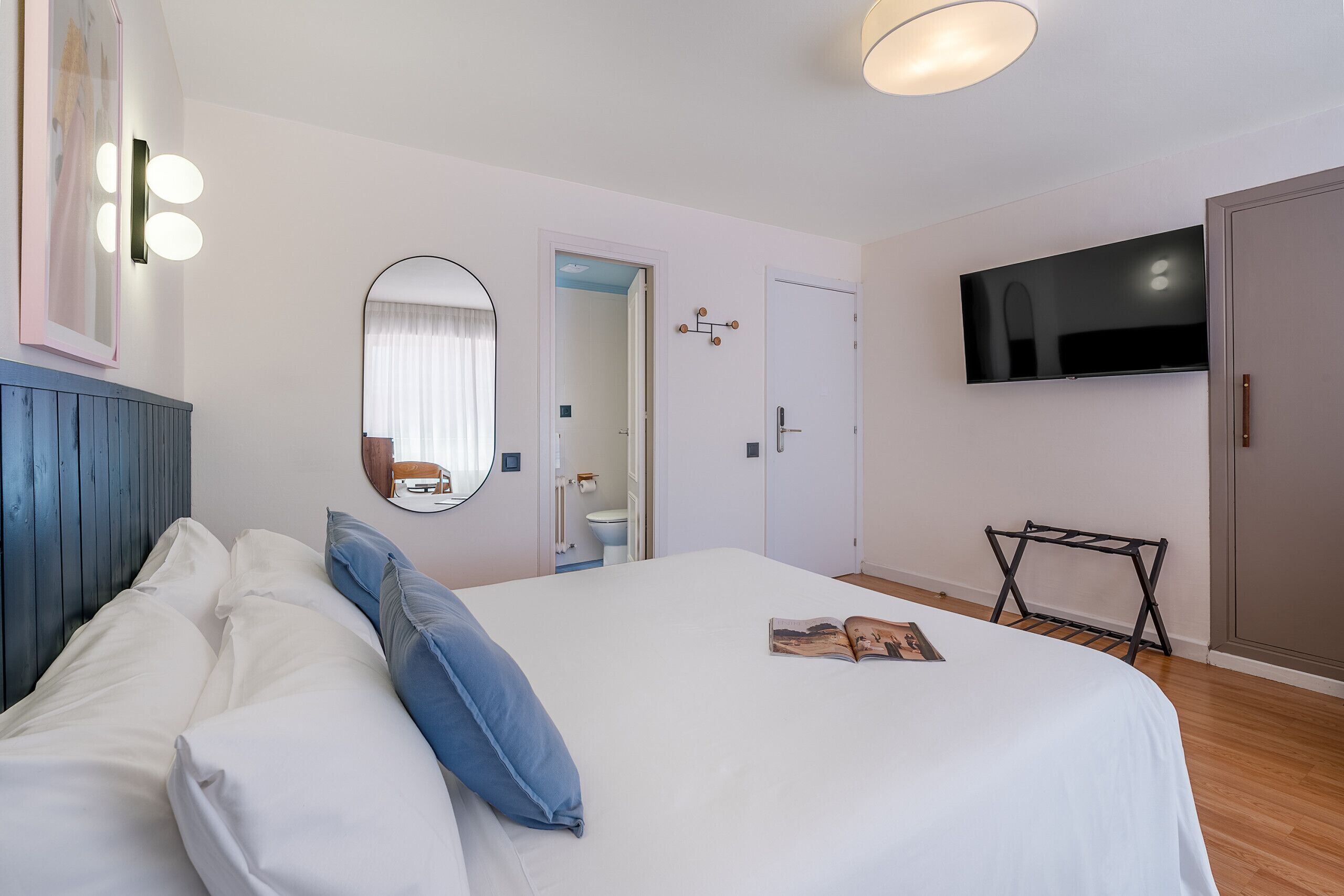 A hotel room with a bed, a TV mounted on the wall, a mirror, and a door leading to a bathroom.