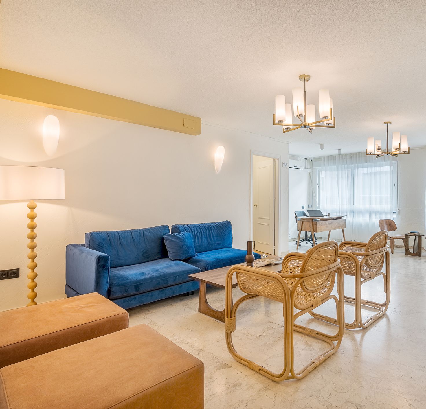 Una sala de estar moderna con un sofá azul, sillas de mimbre, una mesa de centro y una zona de comedor con una computadora portátil.
