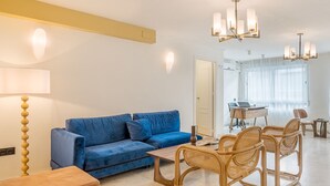 Una sala de estar moderna con un sofá azul, sillas de mimbre, una mesa de centro y una zona de comedor con una computadora portátil.