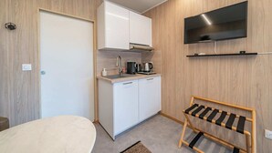 A compact kitchen with white cabinets, a coffee maker, and a TV mounted above the counter.