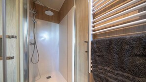 A modern bathroom with a glass-enclosed shower, a wooden vanity, and a towel rack with a dark towel.