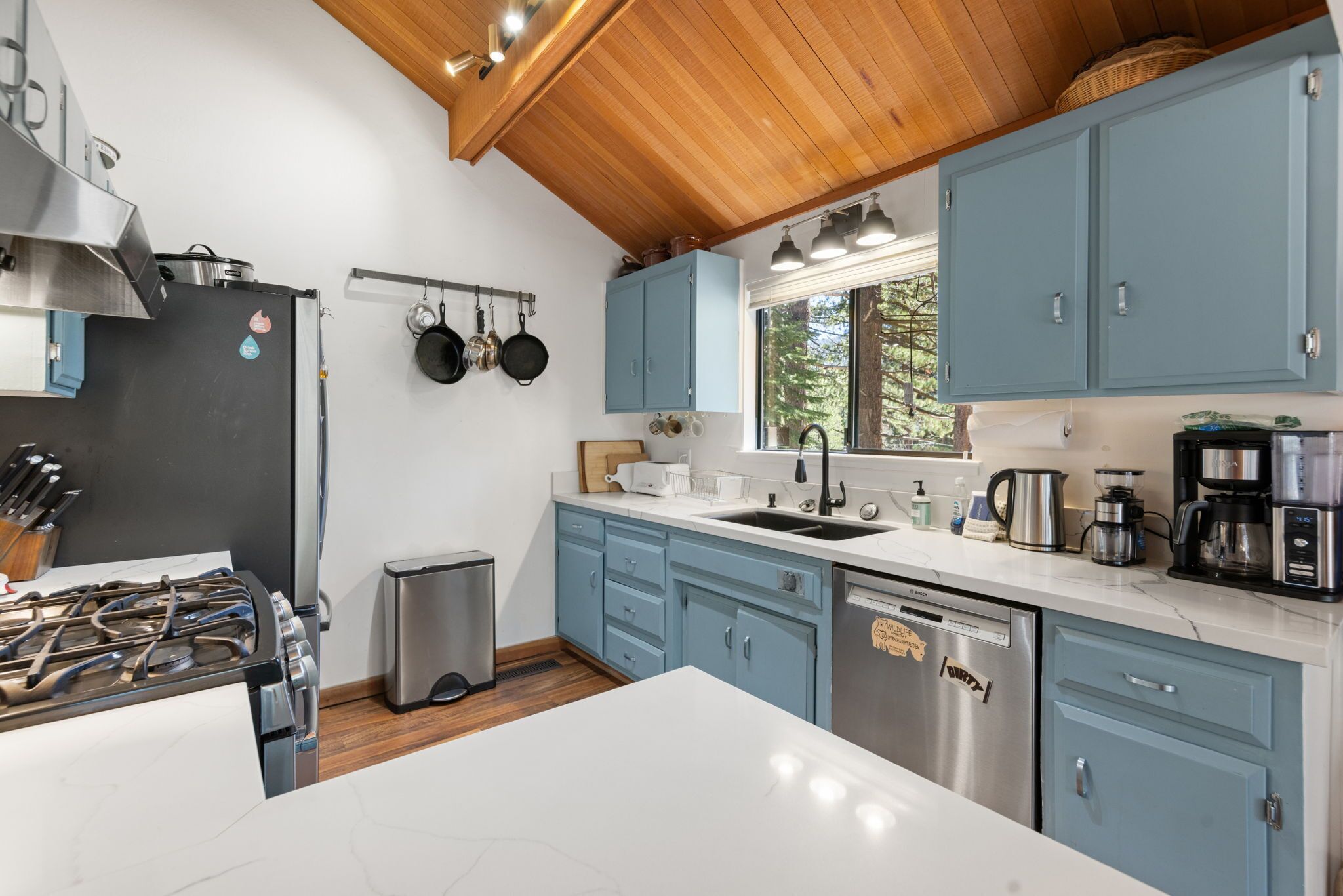 A modern kitchen with a gas stove, stainless steel appliances, blue cabinets, and a wooden ceiling.