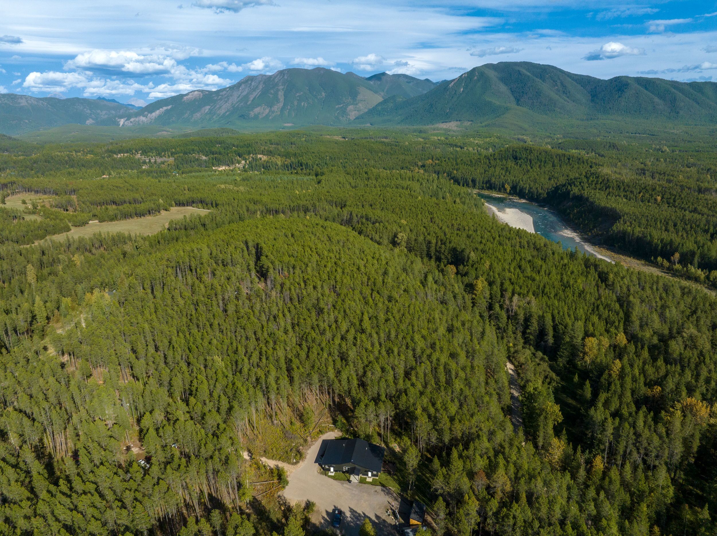 Une vue aérienne d’une zone boisée, avec un petit bâtiment entouré d’arbres denses et une rivière.