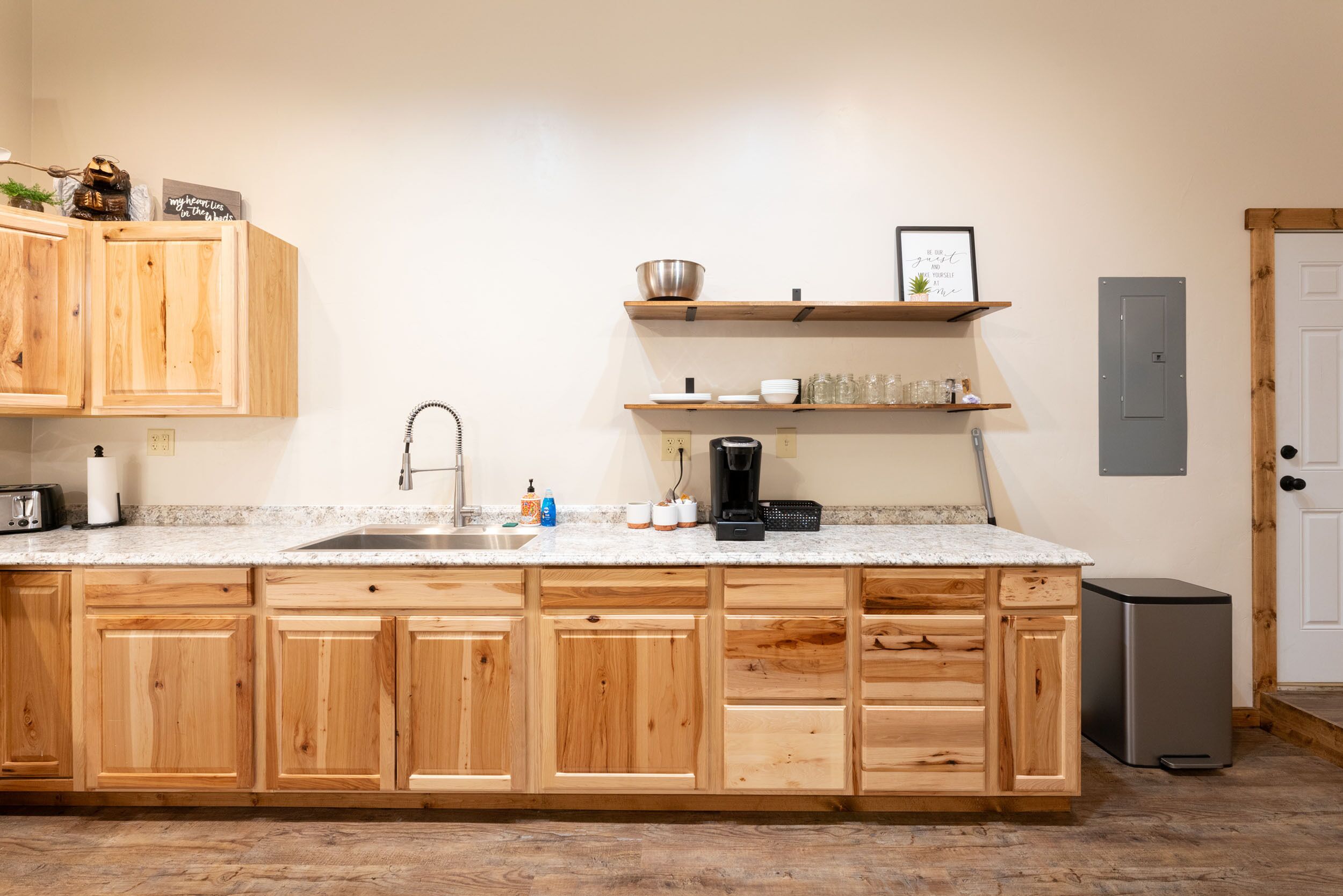A kitchen with wooden cabinets, a granite countertop, a sink, a coffee maker, and a trash can.