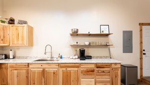 Een keuken met houten kastjes, een granieten aanrecht, een spoelbak, een koffiezetapparaat en een vuilnisbak.