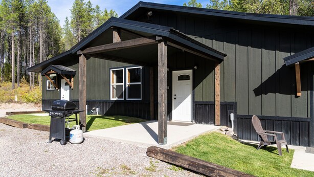 Een chalet met een overdekte veranda, een barbecue en een stoel buiten.