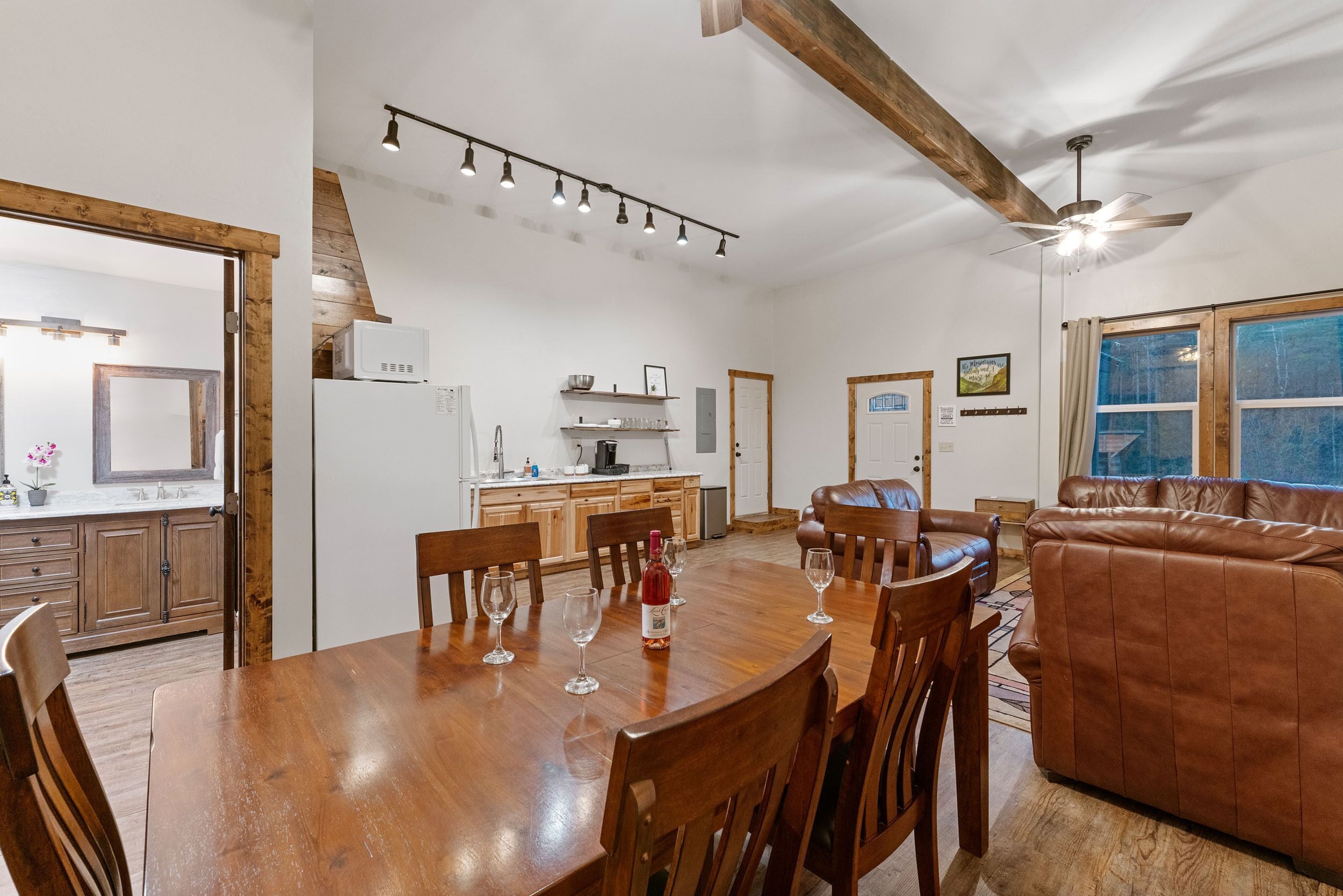 A spacious living area with a wooden dining table, leather sofa, and a kitchen in the background.