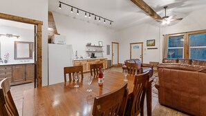 Een ruime woonkamer met een houten eettafel, een leren bank en een keuken op de achtergrond.