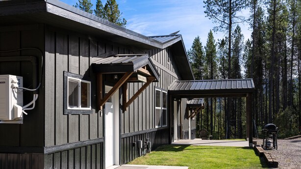 A cabin with a covered porch, a small deck, and a gravel driveway. - North Fork of Spotted Bear Retreat (Columbia Falls)
