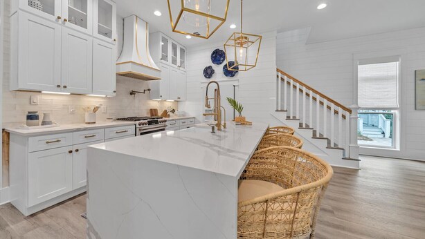 A modern kitchen with white cabinetry, a large island, and a staircase leading to a balcony. - Amazing Location, Golf Cart, Gorgeous New Construction! (Santa Rosa Beach)