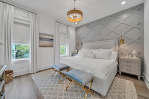 Quarto com cama grande, um banquinho, uma mesinha de cabeceira e um lustre.