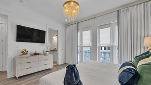 A spacious bedroom with a large bed, a dresser, a TV, and a balcony view. - Amazing Location, Golf Cart, Gorgeous New Construction! (Santa Rosa Beach)