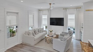 A modern living room with a white sofa, a coffee table, and a TV. - Amazing Location, Golf Cart, Gorgeous New Construction! (Santa Rosa Beach)