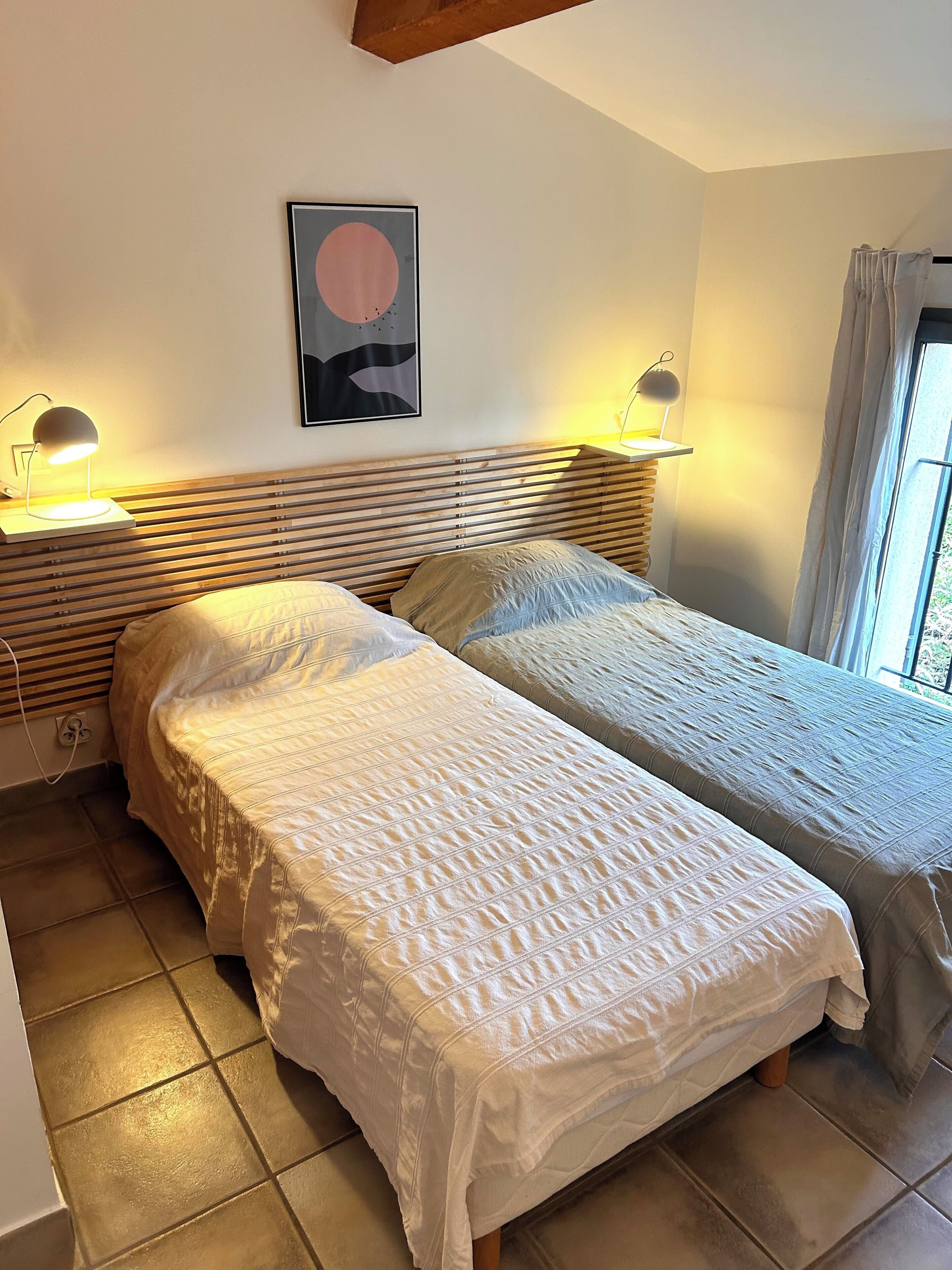 A bedroom with two beds, a wooden headboard, a painting, and bedside lamps.