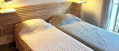 A bedroom with two beds, a wooden headboard, a painting, and bedside lamps.