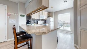 Una cocina con encimera de granito, sillas de madera y vistas a la ciudad a través de amplias ventanas.