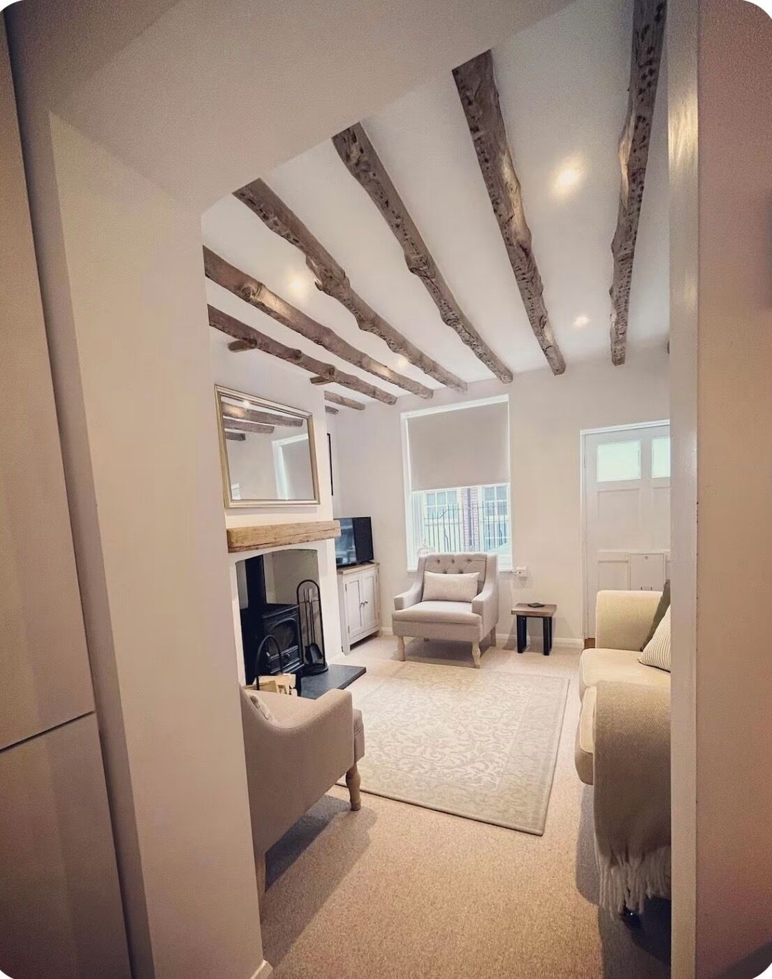Een moderne woonkamer met zichtbare houten balken, een bank, een fauteuil, een televisie en een open haard.