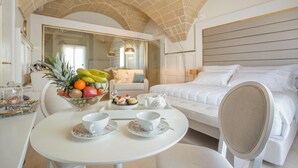 Habitación de hotel con cama, una mesa de comedor con fruta y un juego de té, un espejo y vistas de la habitación.
