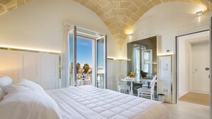 Un dormitorio amplio con una cama grande, un balcón con mesa y sillas, y vistas a palmeras.
