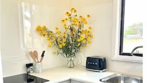 A compact kitchen with white cabinets, a black stove, a toaster, and a vase of yellow flowers on the counter. - Wattle Cottage (Mandurama)