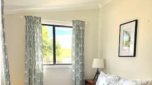 A bedroom with a bed, curtains, a window, a lamp, and a framed picture on the wall. - Wattle Cottage (Mandurama)