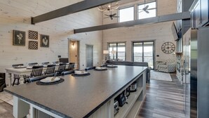 Une cuisine spacieuse dotée d’un grand îlot central, de poutres apparentes en bois au plafond et d’un coin repas avec des chaises et des tables.