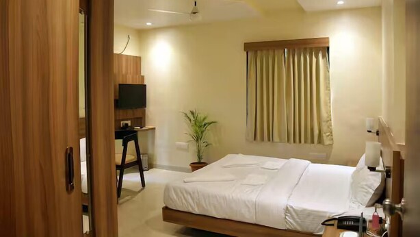 A hotel room with a bed, a desk, a television, a potted plant, and a window with curtains. - The Byke Skylark Seafront Resort, Dapoli (Dapoli)