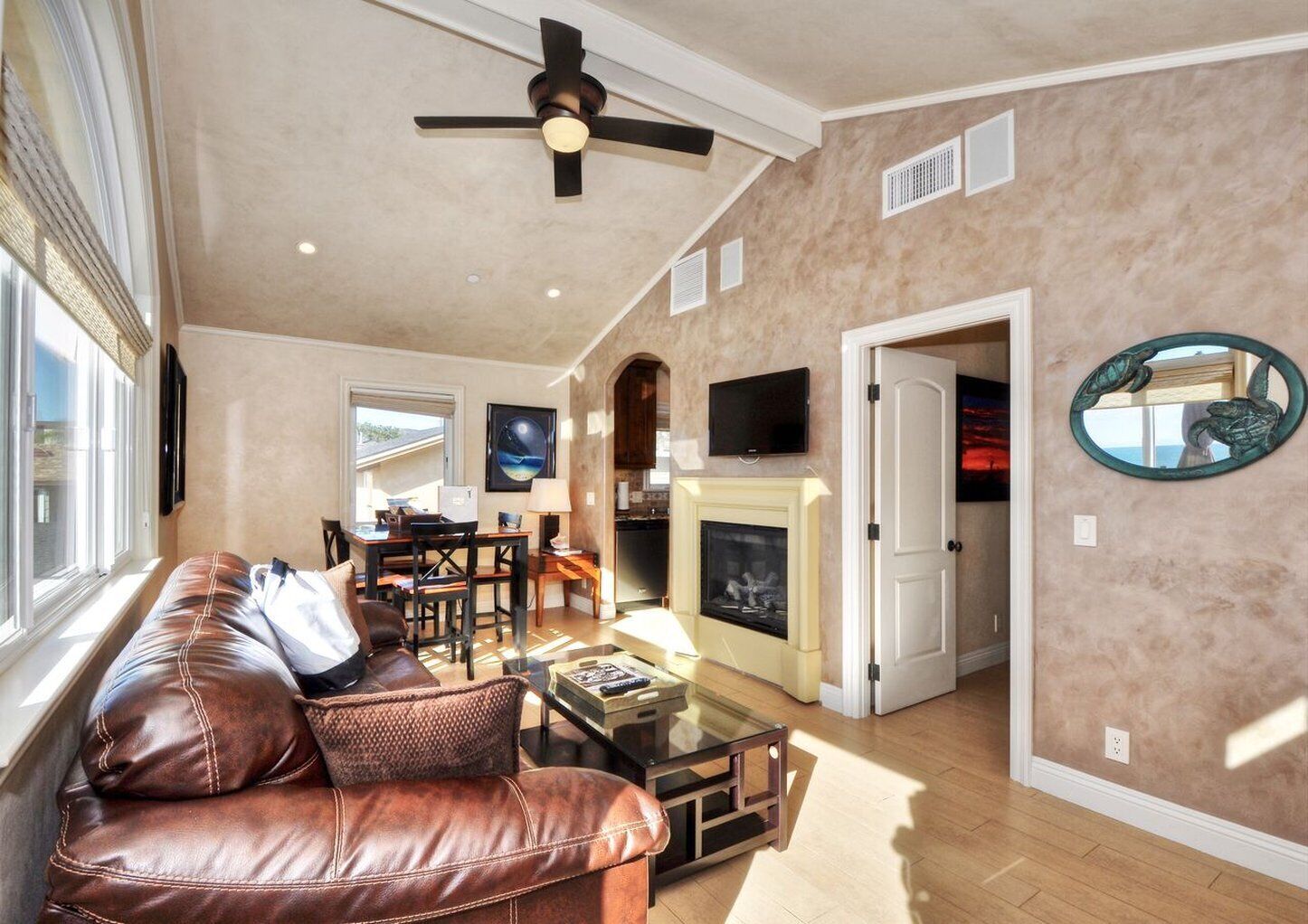 A living room with a leather sofa, a glass coffee table, a fireplace, and a ceiling fan.