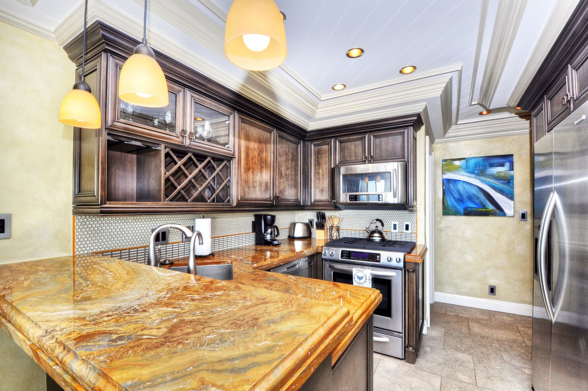 A kitchen with marble countertops, stainless steel appliances, and pendant lighting.