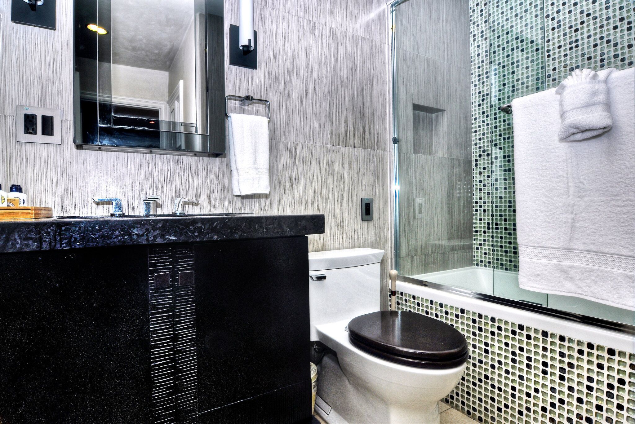 Ein modernes Badezimmer mit einem schwarzen Marmor-Waschtisch, einer weißen Toilette und einer Duschkabine aus Glas.