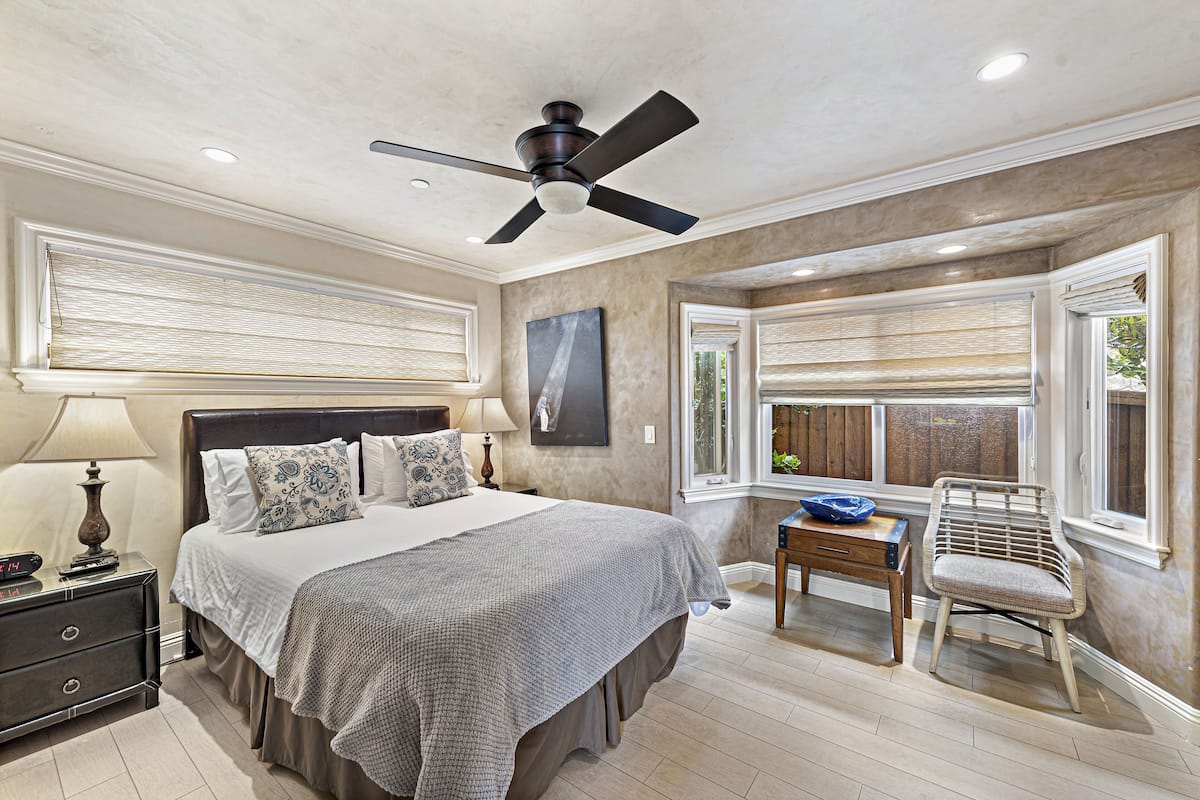A bedroom with a bed, bedside table, lamp, and a ceiling fan.