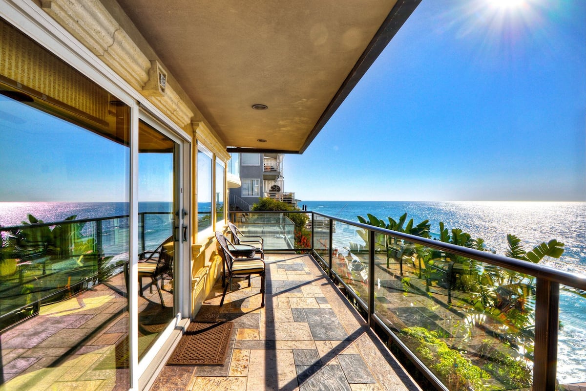 A balcony with a view of the ocean, a seating area with chairs, and a glass railing.