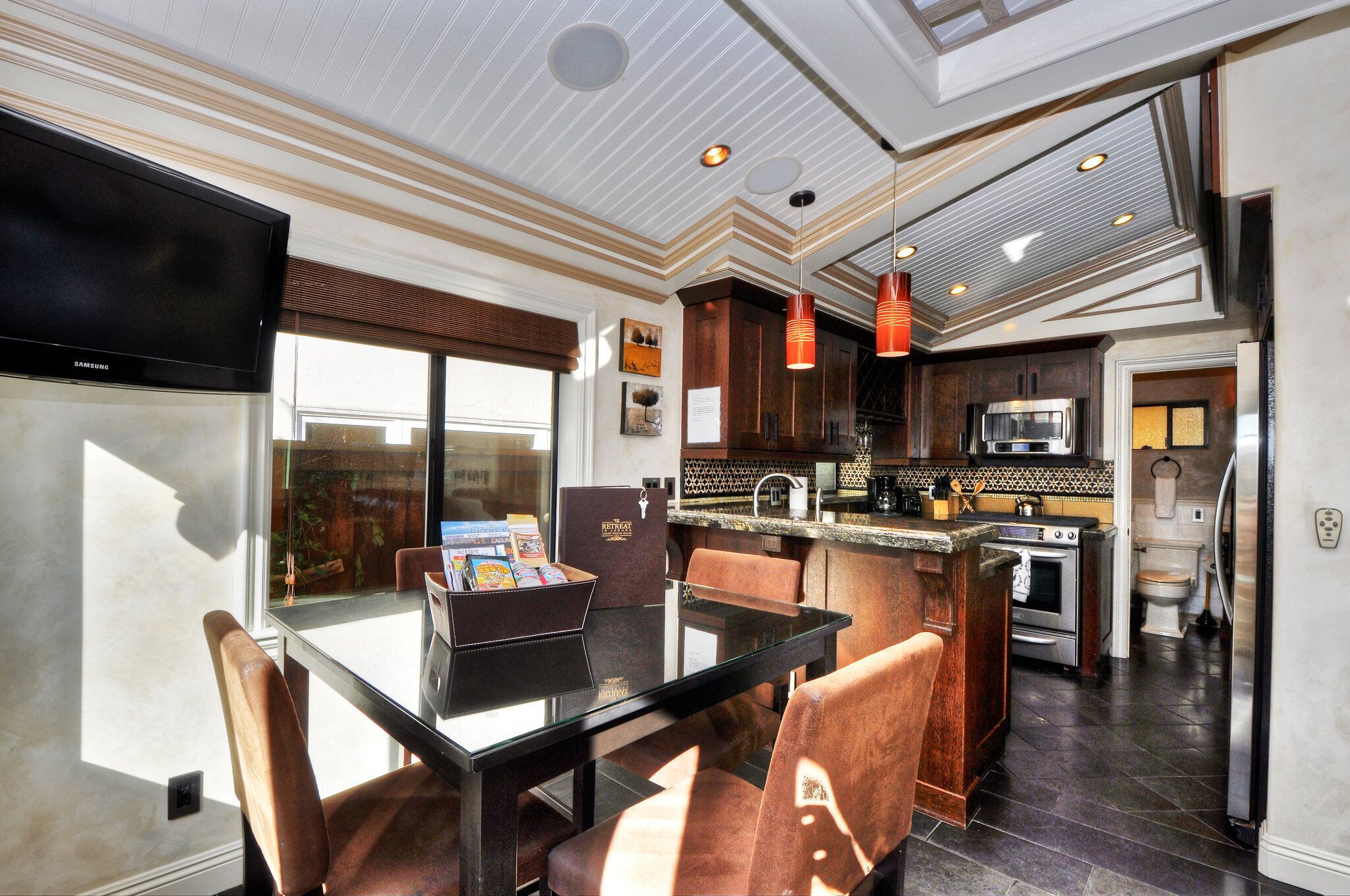 A modern kitchen with a dining area, featuring a large island, built-in appliances, and a flat-screen TV.