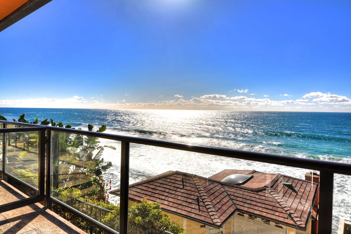 A balcony with a view of the ocean and a building with a tiled roof.