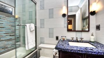 Un baño moderno con cabina de ducha de vidrio, inodoro blanco, lavabo con encimera de granito azul e iluminación empotrada en la pared sobre el espejo.