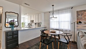 Une cuisine moderne avec des meubles blancs, un coin repas doté d’une table ronde et de chaises noires, et une grande fenêtre ornée de rideaux légers.