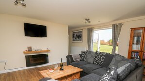 A living room with a sectional sofa, a flat-screen TV, a fireplace, and a view of the outdoors. - Brynteg Cottage (Llanfyrnach)