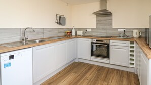 A modern kitchen with white cabinets, a wooden countertop, a built-in oven, and a dishwasher. - Brynteg Cottage (Llanfyrnach)