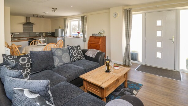 A living room with a sectional sofa, wooden coffee table, and a view of the kitchen and dining area. - Brynteg Cottage (Llanfyrnach)