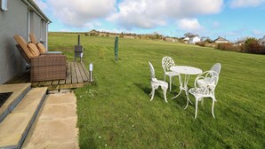 A patio with wicker furniture and a table, a grassy lawn, and a view of the countryside. - Brynteg Cottage (Llanfyrnach)