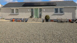 A two-story building with a green door, solar panels on the roof, and a gravel driveway. - Brynteg Cottage (Llanfyrnach)