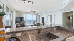 A modern kitchen with a granite countertop, stainless steel sink, and a ceiling fan. - Beachfront, 4th floor, Wrap Balcony, Great Views! (Panama City Beach)