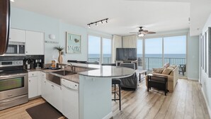 A modern kitchen with a central island, a dining area with a view of the ocean, and a balcony with a view of the beach. - Beachfront, 4th floor, Wrap Balcony, Great Views! (Panama City Beach)