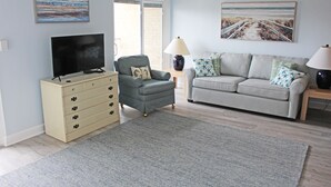 Una sala de estar con televisión, sofá, sillón y lámpara.