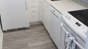 Una cocina con gabinetes blancos, un refrigerador, un lavavajillas, un fregadero y una estufa.
